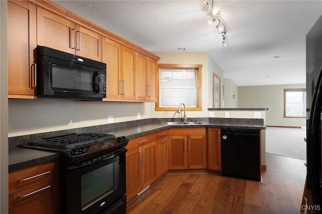 kitchen with sink, rail lighting, dark wood-type flooring, kitchen peninsula, and black appliances