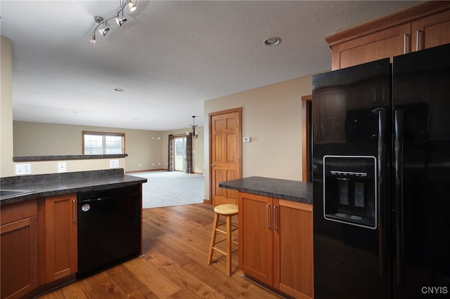 kitchen featuring sink, light hardwood / wood-style flooring, track lighting, a breakfast bar, and black appliances