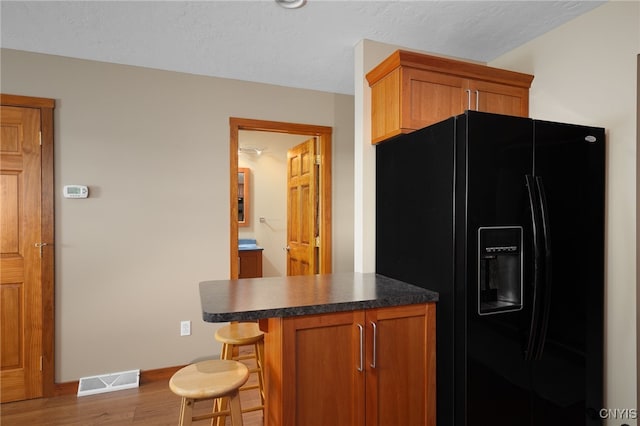 kitchen with a kitchen bar, kitchen peninsula, black refrigerator with ice dispenser, and light hardwood / wood-style flooring