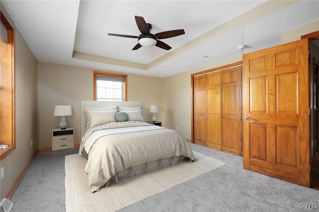 carpeted bedroom with a closet, a raised ceiling, and ceiling fan