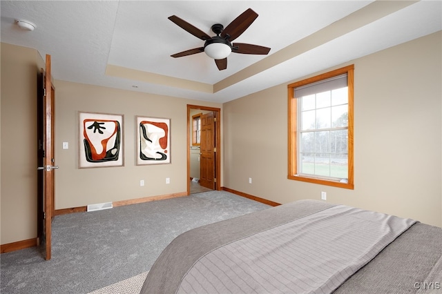 carpeted bedroom featuring a tray ceiling and ceiling fan