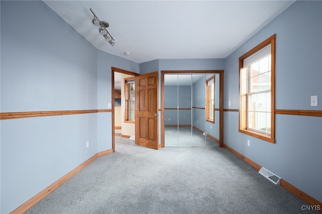 unfurnished bedroom featuring light carpet, rail lighting, and a closet