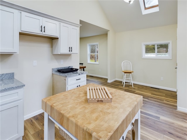 kitchen featuring vaulted ceiling with skylight, a healthy amount of sunlight, and white cabinetry