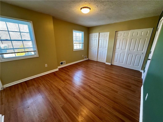 unfurnished bedroom with a textured ceiling, dark wood-type flooring, multiple windows, and multiple closets