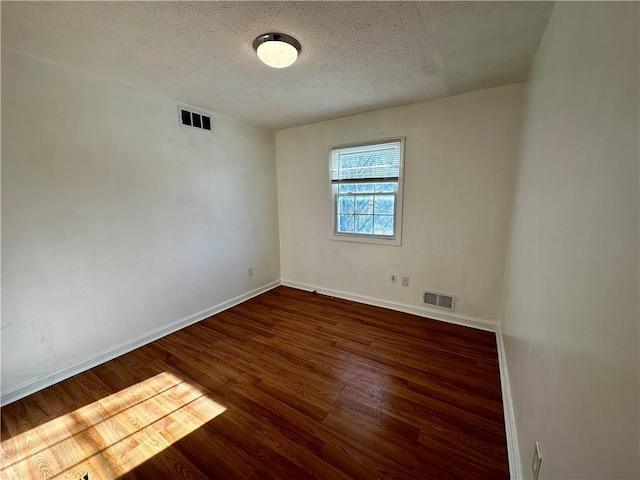 spare room featuring a textured ceiling and dark hardwood / wood-style floors