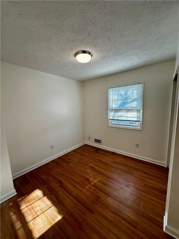 empty room with dark hardwood / wood-style flooring and a textured ceiling