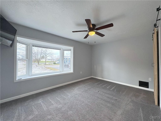 spare room featuring a textured ceiling, dark carpet, and ceiling fan