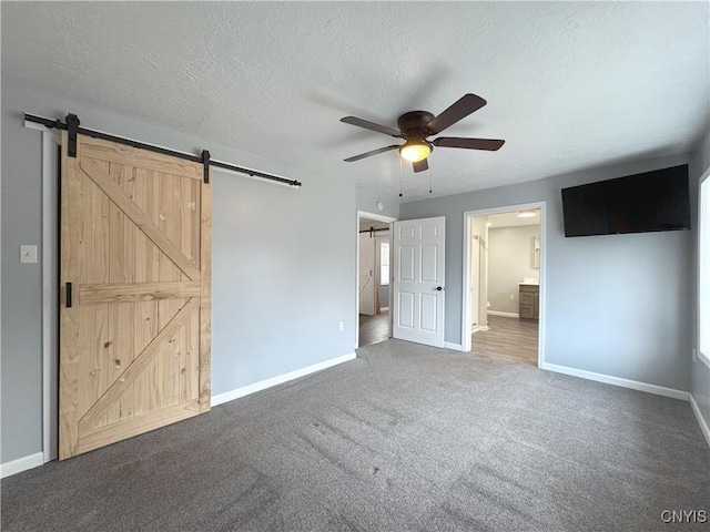 unfurnished bedroom with carpet flooring, ceiling fan, a barn door, ensuite bathroom, and a textured ceiling