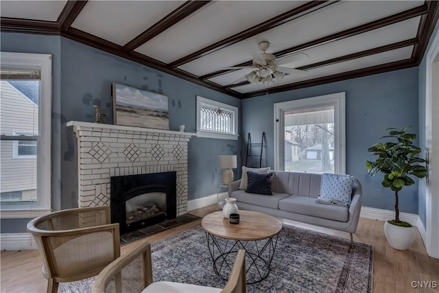 living room featuring crown molding, ceiling fan, light wood-type flooring, a fireplace, and beam ceiling