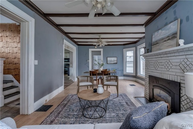 living room featuring a fireplace, beamed ceiling, ornamental molding, and light hardwood / wood-style flooring