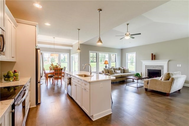 kitchen with a center island with sink, sink, hanging light fixtures, appliances with stainless steel finishes, and white cabinetry