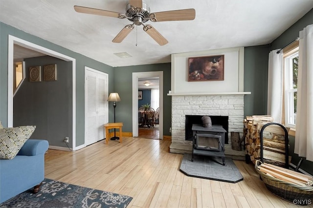 living room with a wood stove, light hardwood / wood-style flooring, and ceiling fan