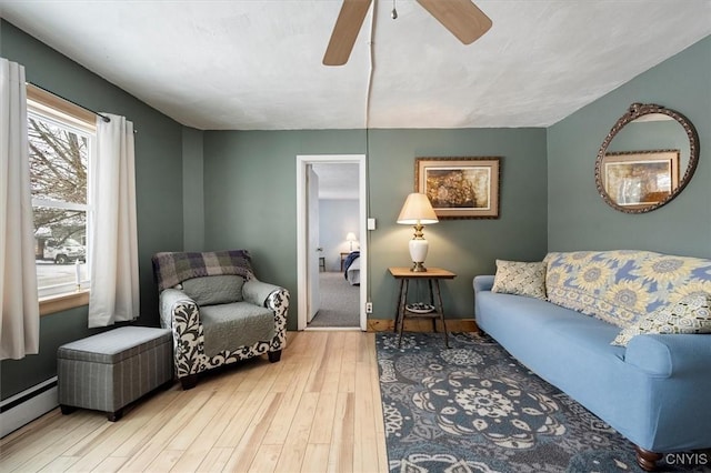 living area with a baseboard radiator, hardwood / wood-style flooring, and ceiling fan