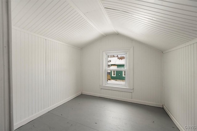 additional living space with concrete floors, lofted ceiling, and wood walls