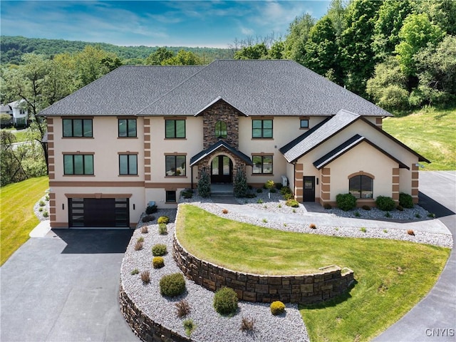 view of front of house with stucco siding, a front yard, a garage, stone siding, and driveway