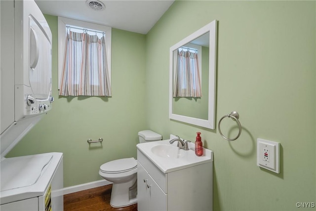 bathroom with hardwood / wood-style floors, vanity, toilet, and stacked washer / dryer