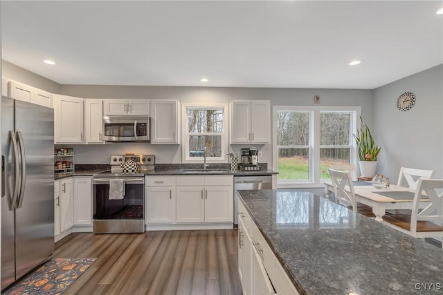 kitchen with white cabinets, sink, dark hardwood / wood-style floors, dark stone countertops, and stainless steel appliances