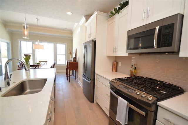 kitchen featuring white cabinets, crown molding, sink, appliances with stainless steel finishes, and decorative light fixtures