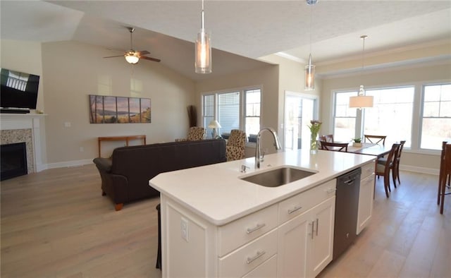 kitchen featuring a tile fireplace, sink, hanging light fixtures, an island with sink, and white cabinets