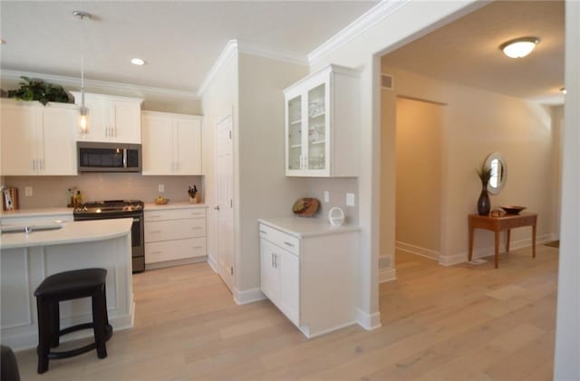 kitchen with stainless steel appliances, light hardwood / wood-style flooring, crown molding, a kitchen bar, and white cabinets