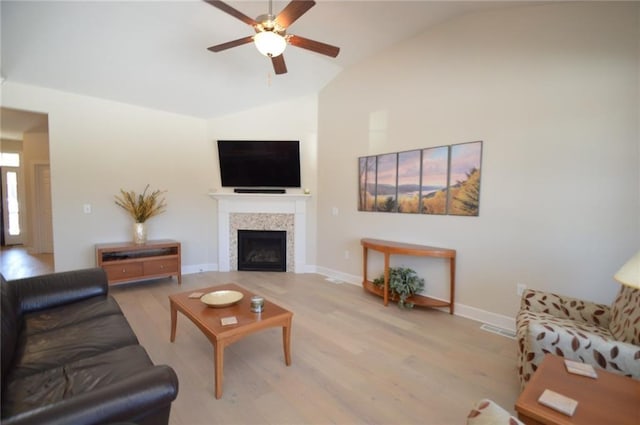 living room featuring ceiling fan, a fireplace, lofted ceiling, and light wood-type flooring