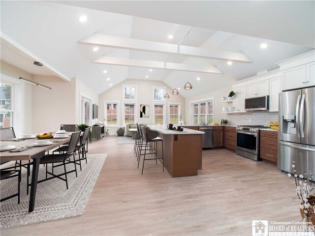 kitchen with appliances with stainless steel finishes, tasteful backsplash, pendant lighting, white cabinets, and a center island