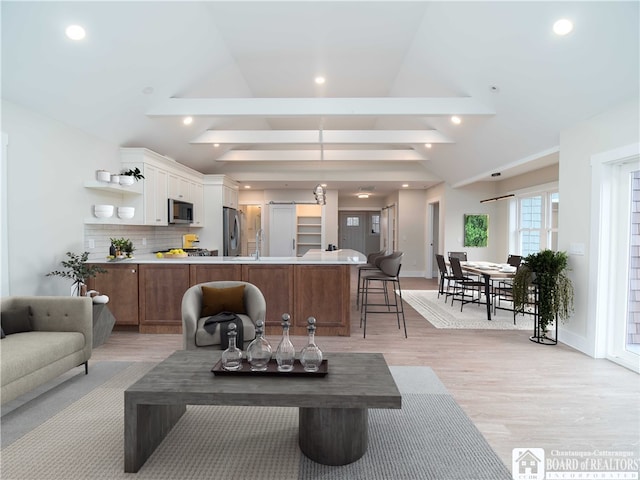 living room with lofted ceiling with beams, light hardwood / wood-style flooring, and sink