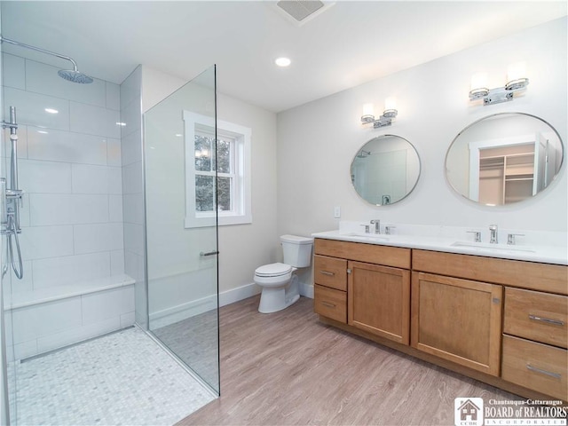 bathroom featuring vanity, wood-type flooring, toilet, and tiled shower