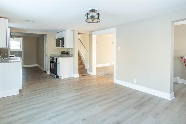 kitchen featuring white cabinets, light wood-type flooring, light stone countertops, and stainless steel range with electric stovetop