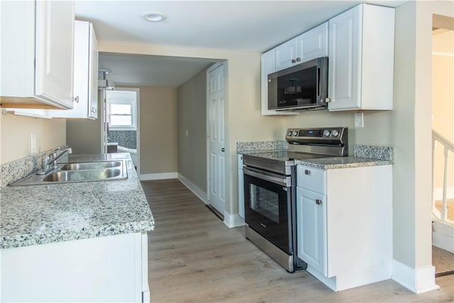 kitchen featuring sink, light stone counters, light hardwood / wood-style floors, white cabinets, and appliances with stainless steel finishes