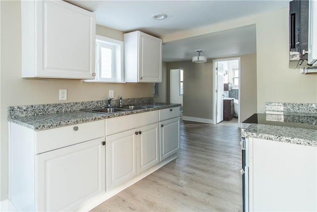 kitchen featuring light stone countertops, sink, white cabinets, and light hardwood / wood-style floors