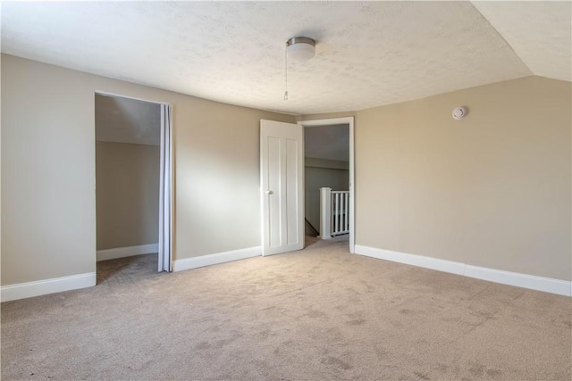 unfurnished bedroom featuring carpet, a textured ceiling, and vaulted ceiling