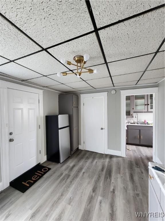 unfurnished living room with a paneled ceiling, sink, and light hardwood / wood-style floors