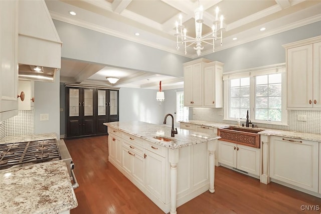 kitchen featuring sink, light stone counters, pendant lighting, and an island with sink