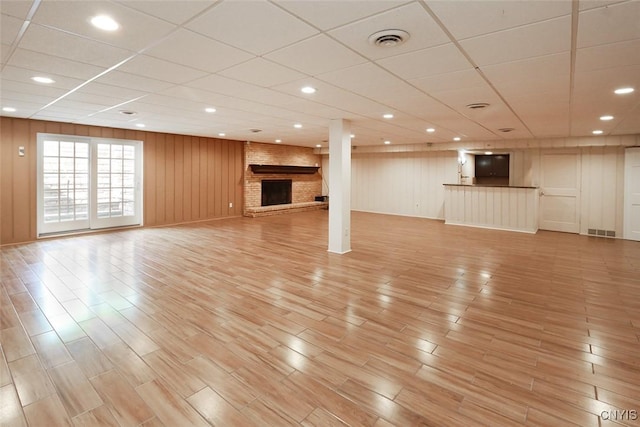 unfurnished living room featuring a paneled ceiling, wooden walls, and a fireplace