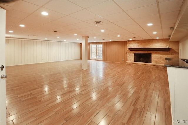 interior space with a brick fireplace, light hardwood / wood-style floors, and a drop ceiling