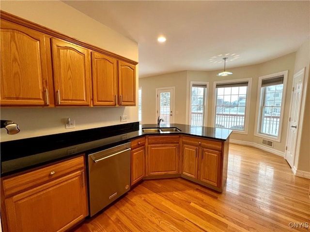 kitchen with kitchen peninsula, stainless steel dishwasher, sink, pendant lighting, and light hardwood / wood-style flooring