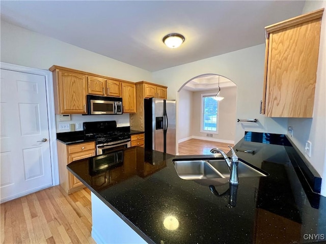 kitchen featuring dark stone countertops, sink, stainless steel appliances, and light hardwood / wood-style floors