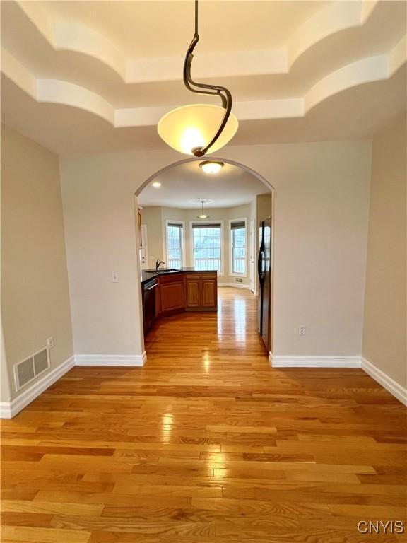 unfurnished dining area featuring a tray ceiling, light hardwood / wood-style flooring, and sink