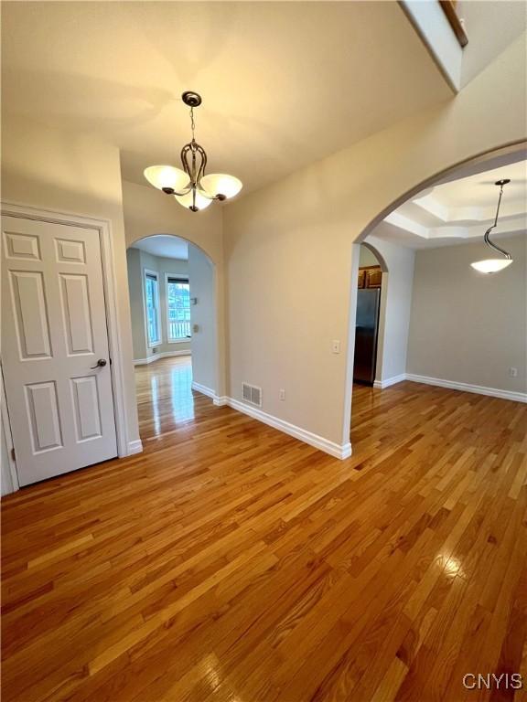 interior space with a notable chandelier, a raised ceiling, and wood-type flooring