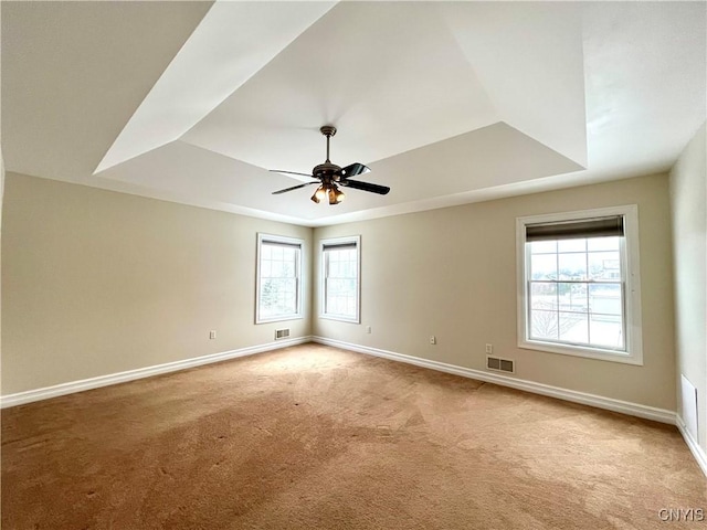 spare room with a raised ceiling, ceiling fan, and light colored carpet