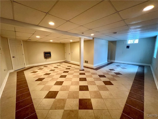 basement featuring a paneled ceiling and heating unit