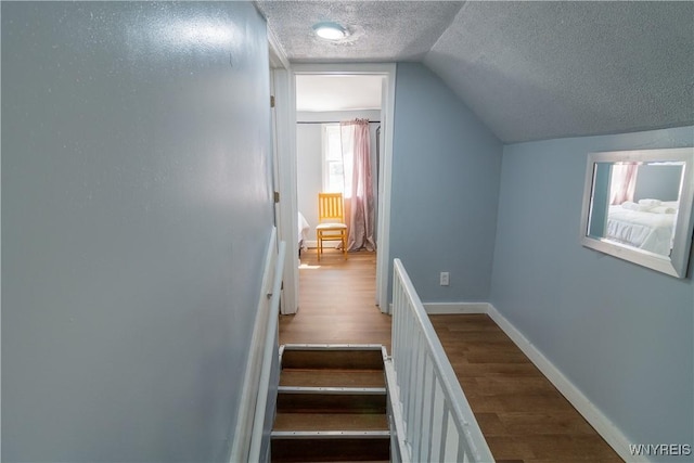 stairway featuring lofted ceiling, hardwood / wood-style floors, and a textured ceiling