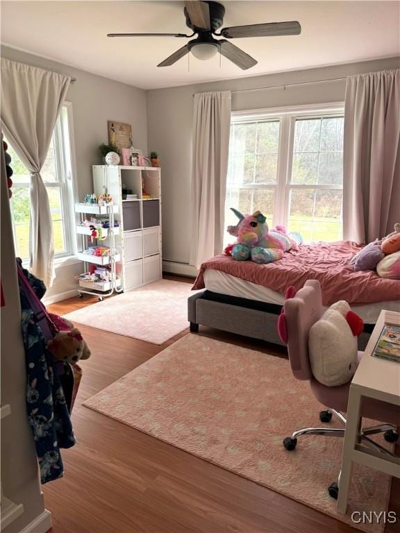 bedroom with hardwood / wood-style flooring, ceiling fan, and a baseboard heating unit