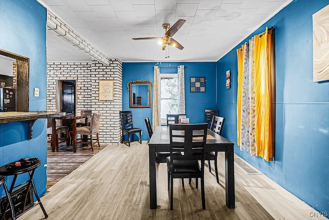 dining room with ceiling fan, hardwood / wood-style floors, and brick wall