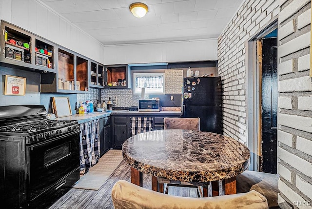 kitchen with black appliances, hardwood / wood-style floors, and brick wall