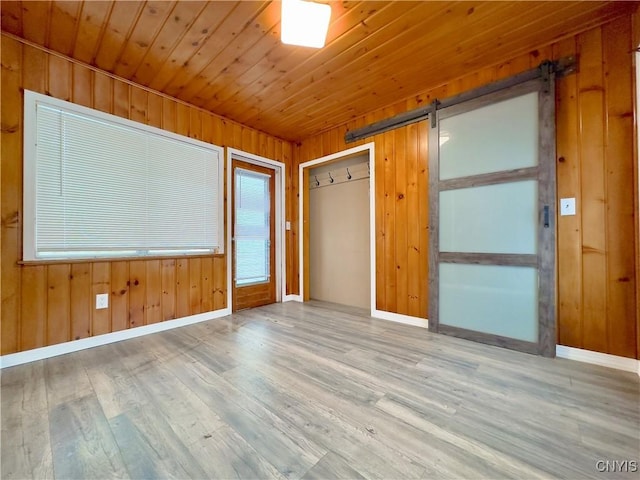 empty room featuring a barn door, wooden walls, wood ceiling, and light hardwood / wood-style floors