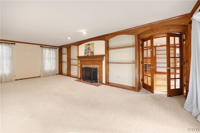 unfurnished living room featuring a fireplace, french doors, light colored carpet, and crown molding