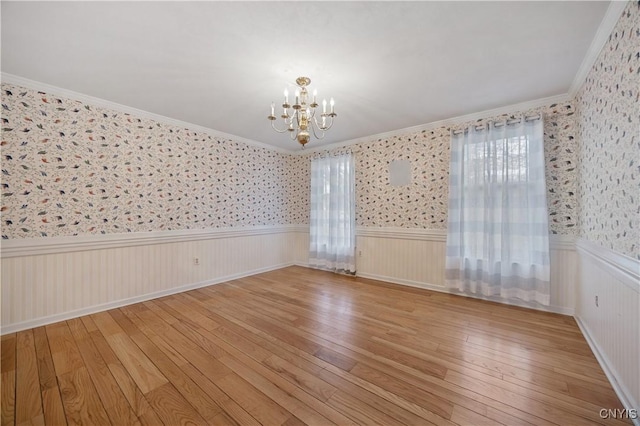 empty room featuring crown molding, light hardwood / wood-style flooring, and a chandelier