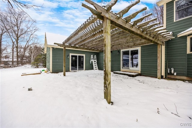 snow covered back of property with a pergola